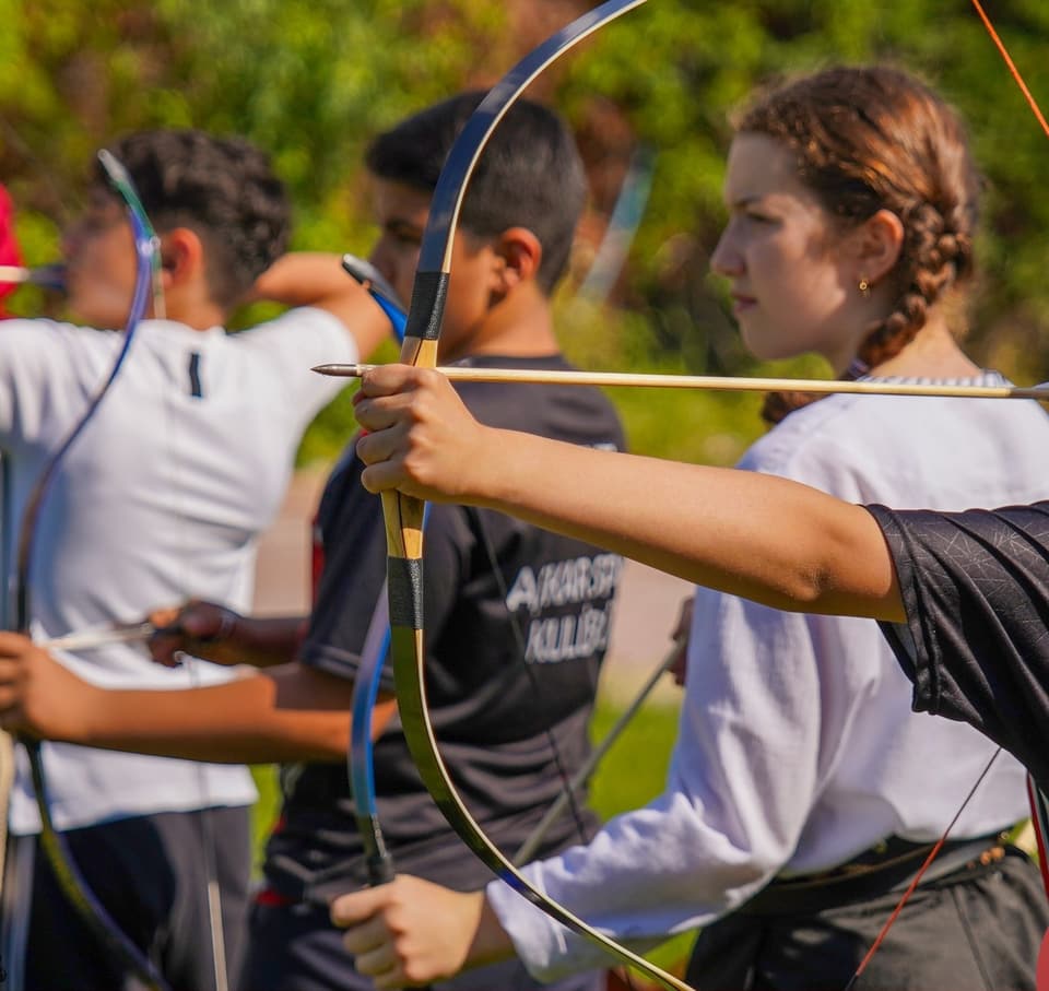 Açık alanda yan yana geleneksel yaylarla çekiş yapan sporcular