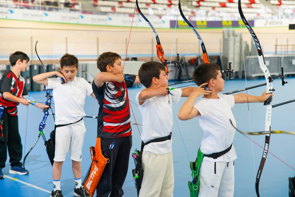 Sıra hâlinde çekiş yapan genç sporcular, olimpik yaylarla